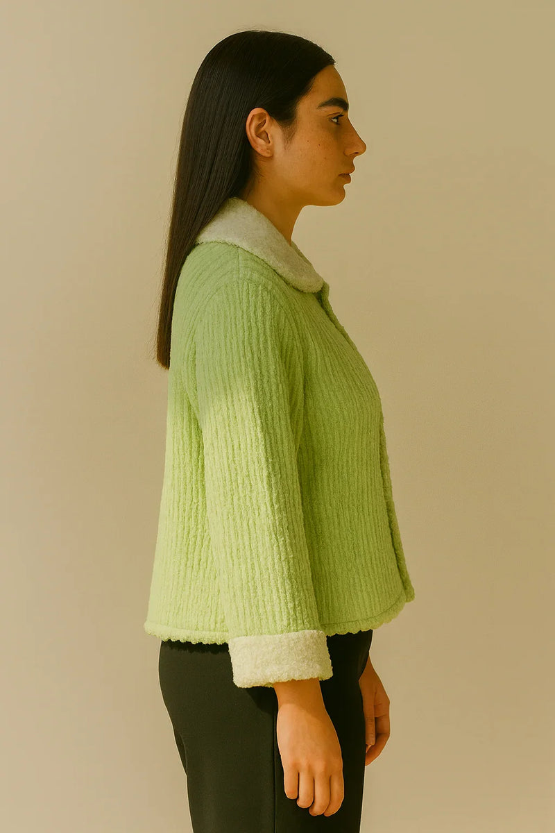 Woman wearing a green ribbed sweater with a beige collar against a beige background