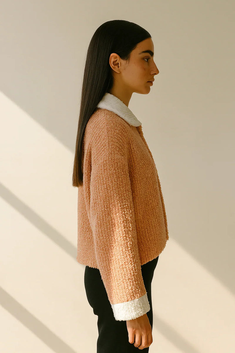Woman wearing a pink textured sweater with white trim against a neutral background