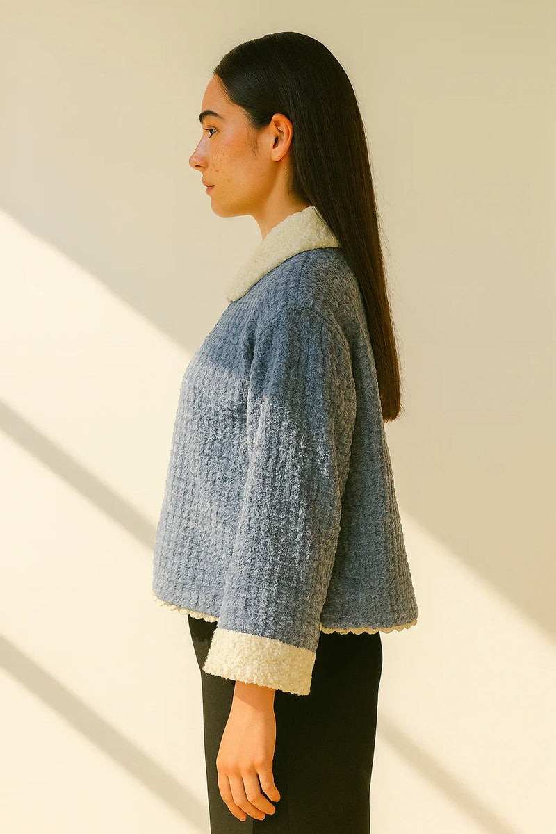 Woman wearing a textured blue jacket with a neutral background